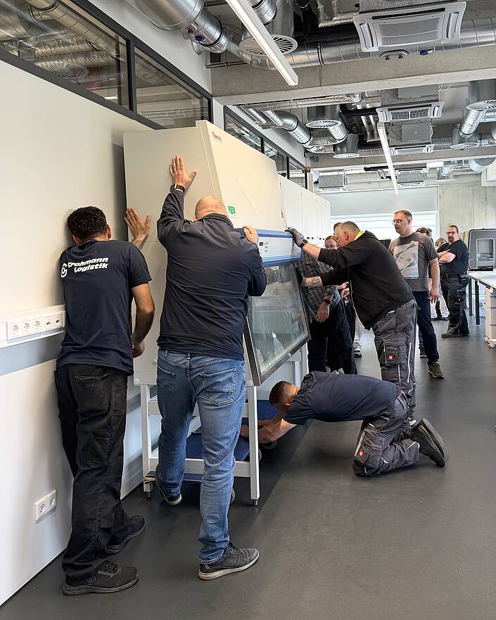 Ein technisches Großgerät wird von mehreren Personen an einer Wand platziert.