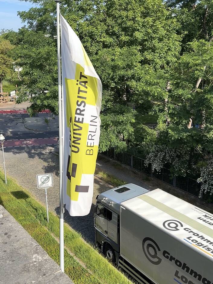 Fahne der FU Berlin, im Hintergrund Umzugswagen